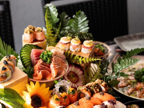 Mesa com variedade de sushi, decorada com folhas verdes e flores, em apresentação elegante.